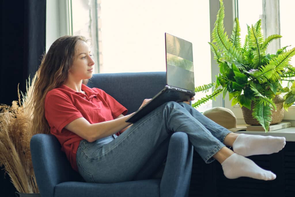 young female using laptop after work, communicates on internet with customer. happy freelance woman is relaxing on comfortable couch and using laptop at home.